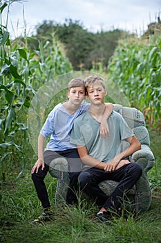 Two brothers sitting on a armchair in a field in the countryside in summer day