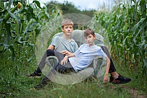 Two brothers sitting on a armchair in a field in the countryside in summer day