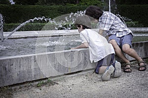 Two brothers are sitting in a summer park near a fountain and playing in the water. Family have fun.