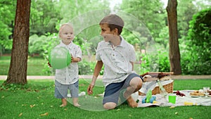 Two brothers spending time in summer park. Siblings playing with ball outdoors