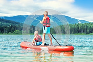 Two brothers swimming on stand up paddle board.Water sports , active lifestyle.