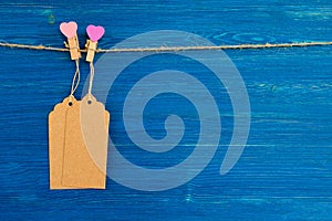 Blank paper price tags or labels set and wooden pins decorated on hearts hanging on a rope on the blue wooden background.