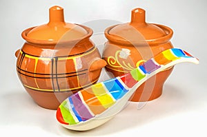 Two brown clay pots with colored ceramic spoon on white background