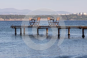 Two Brown wooden tables with chairs are on the bridge on the seaside in the evening