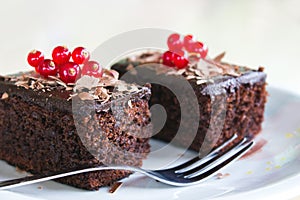 Two brownies with redberries on top, served in a plate on a wooden table
