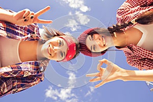 Two Brunette teenage girls friends in hipster outfit (jeans shorts, keds, plaid shirt, hat) with a skateboard at the park outdoors