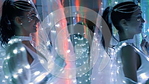 Two brunette woman in costumes of white LEDs among mirrors