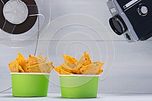 Two buckets with nachos, on a gray background, next to an old video camera and a film