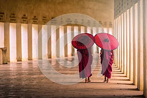 Two buddhist monk novice holding red umbrellas and walking in pa