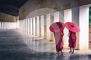 Two buddhist monk novice holding red umbrellas and walking in pagoda, Myanmar