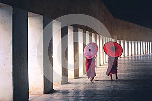 Two buddhist monk novice holding red umbrellas and walking in pagoda, Myanmar