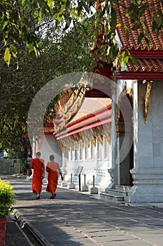 Two Buddhist monks are walking along the main hall of Wat Benchamabophit in Bangkok (Thailand) photo