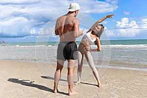 Two buddy doing body stretching exercises outdoor on summer tropical island beach with blue sea, couple doing exercise outdoor,