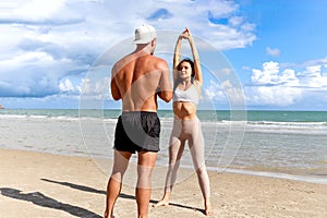 Two buddy doing body stretching exercises outdoor on summer tropical island beach with blue sea, couple doing exercise outdoor,