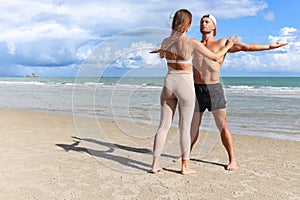 Two buddy doing body stretching exercises outdoor on summer tropical island beach with blue sea, couple doing exercise outdoor,