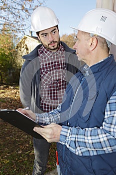 Two builders in hardhats with clipboard outdoors