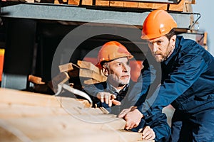 two builders in helmets working with wooden planks outside