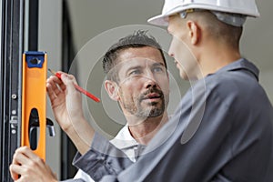 Two builders talking while holding spirit level against window