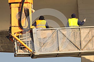 Two builders in yellow at the construction site work on crane