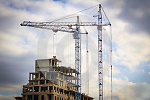 Two building cranes in front of the building under construction against a sky with clouds