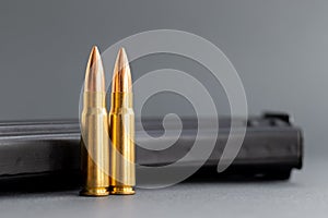 Two bullets against Kalashnikov assault rifle clip, magazine on blurred gray background. Cartridges 7.62 caliber for ak 47,