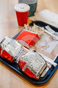 Two burgers wrapped in tinfoil, french fries potato chips, red cup of coffee