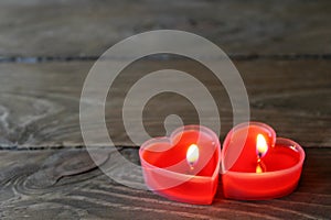 Two burning candles in the chape of a red heart are isolated  on a brown background.