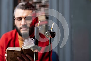 Two burning candles standing on table near diviner reading book