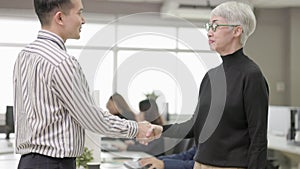Two business associates rise and shake hands to express their willingness to work together. In the workplace
