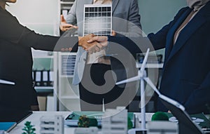 Two business executives, elegantly attired in suits, join hands in a gesture of unity, solidarity, and shared commitment towards a photo