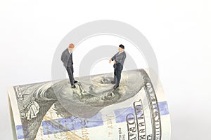 Two business man mannequins discussing while standing on dollar bills