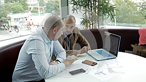 Two business men sit at a laptop and monitor the development of business. Business