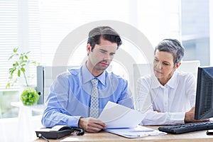 Two business people looking at a paper while working on computer