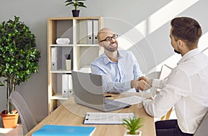 Two business people in office making deal. Two men shaking hands celebrating business achievement.