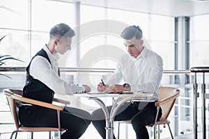 Two business people sign documents in a large, spacious office