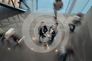 Two business people standing in busy office with a blur of people walking past