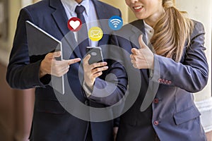 Two business people standing in office and using social media network on mobile smart phone