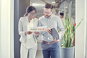 Two business people working together with documents while having informal meeting in office hallway