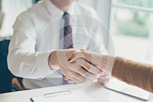 Two business point a pen to each other above blank paper at meeting