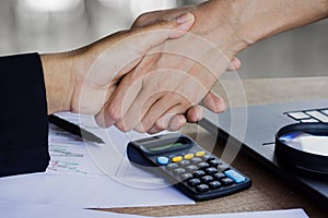 Two business woman handshake after working together and agree on their project at office with some financial paper graph