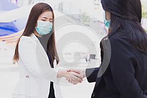 Two business woman wearing mask and making handshake in the city. Business etiquette, social distance concepts