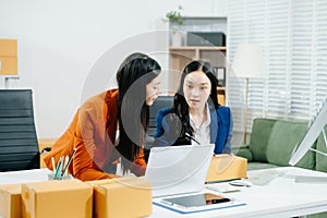 Two business women collaborate in a modern office, working on e-commerce packaging and startup ideas with laptops, teamwork