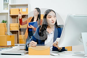 Two business women collaborate in a modern office, working on e-commerce packaging and startup ideas with laptops, teamwork