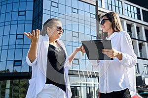 Two business women discussing some questions outside office building