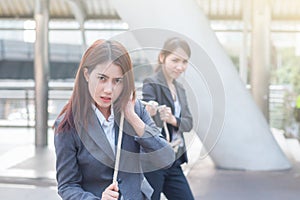 Two business women pulling a rope competing with commitment to winer