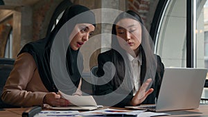 Two business women students girls studying together laptop writing multiracial female multiethnic businesswomen Asian