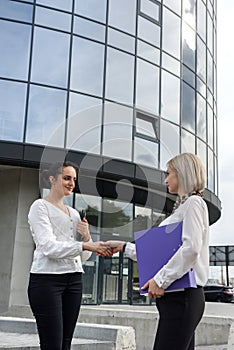 Two business women in suits handshaking before office building
