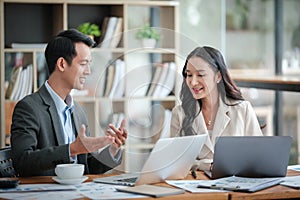 Two business workers smiling happy working sitting on desk at the office.