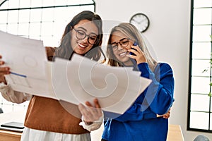 Two business workers woman reading paperwork talking on the smartphone at the office