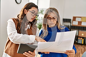 Two business workers woman reading paperwork using touchpad at the office